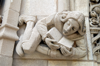 Detail of an architectural stone carving depicting a person reading a book.